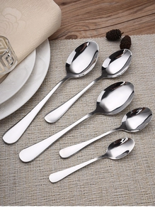 Set of five stainless steel spoons in various sizes arranged on a rustic woven placemat