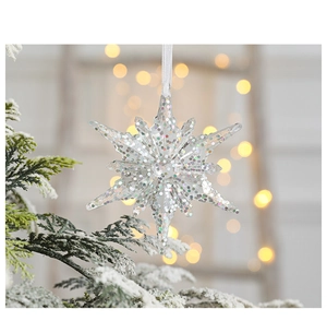 Iridescent acrylic snowflake ornament hanging on a pine branch with warm bokeh lights