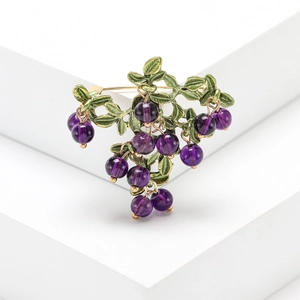 Minimalist cranberry fruit brooch with purple beads and gold metal leaf on white background