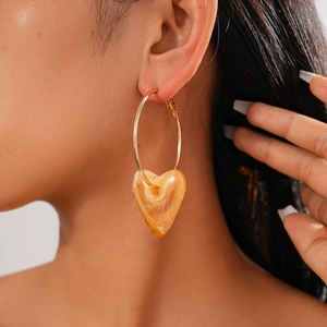 Close-up of a gold hoop earring featuring an amber acrylic heart pendant on a model