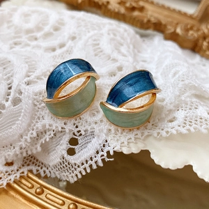 Macro shot of blue and green enamel vintage geometric earrings with gold trim on lace