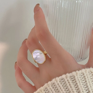 Detail of an oval mother of pearl ring in gold finish worn by a model in a cozy scene