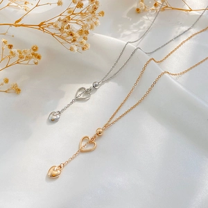 Close-up of gold and silver hollow heart pendant necklaces on white silk fabric