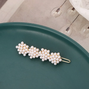 Elegant gold metal hair clip featuring four clustered white pearls on a green display plate