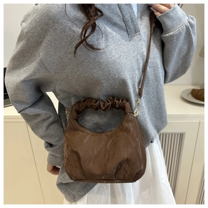Brown ruched cloud bag shown cross-body style on a model in a minimalist interior