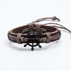 Close-up of vintage braided leather bracelet with black metal ship wheel charm