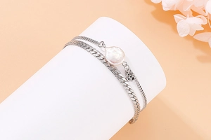 Detail of silver double-layered bracelet with baroque pearl and clover charm on a stand