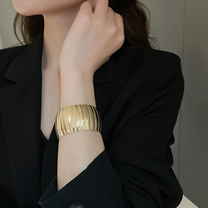 Macro view of a wide gold metal cuff bracelet with vertical texture on black blazer sleeve
