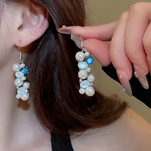 Elegant beaded drop earrings with white pearls and blue beads on a female model