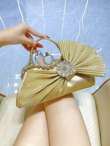 Close-up of golden evening clutch bag featuring a radiant rhinestone flower and crystal ring handle