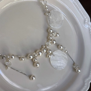 Macro detail of pearl tassel necklace with shell pendants on a white ceramic plate