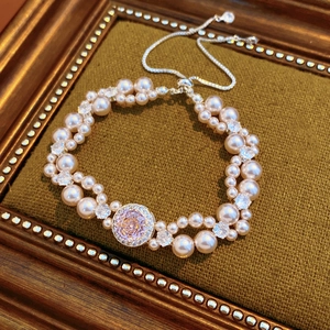 Dettaglio di bracciale di perle rosa con rosa in zircone su cuscino di velluto