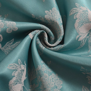 Detail of teal satin jacquard fabric with silver floral rabbit pattern and spiral pleats