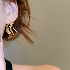 Close-up of a model wearing golden wave-shaped multi-layered hoop earrings in a modern style