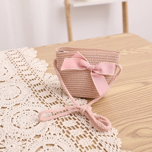 Détail du sac bandoulière en paille rose avec grand nœud sur une table en bois