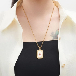 Detail of gold necklace with rectangular rhinestone pendant and red heart on white enamel