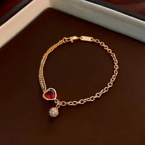 Gold plated bracelet featuring a red heart gemstone and sparkling pavé crystal ball charm