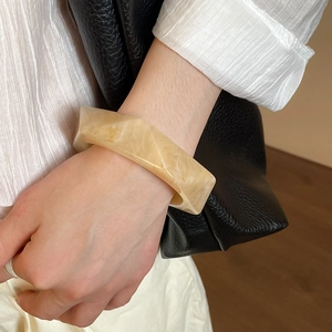 Detail of a wide irregular resin bangle featuring a yellow marble pattern on a model's wrist