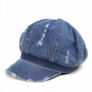 Close-up of distressed blue denim newsboy cap with ripped holes and orange stitching