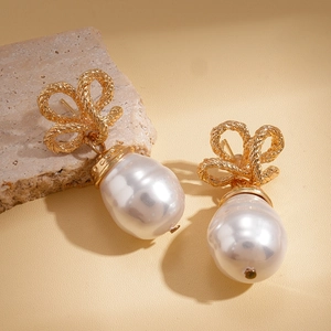 Vintage gold bow earrings with white baroque pearl pendants on beige stone surface