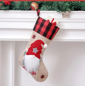 Close-up of beige linen Christmas stocking with gnome and gift box on fireplace