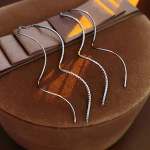 Détail macro de boucles d'oreilles vagues argentées avec fils à pampilles sur coffret