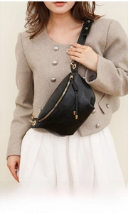 Detail der schwarzen Leder-Brusttasche mit goldenen Beschlägen und Quasten an einem Model getragen