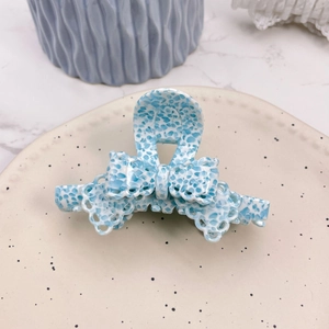 Close-up of a light blue floral acetic acid hair claw clip with a bow design on a tray