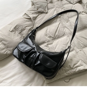 Detailed view of black pleated leather baguette bag with silver hardware on beige coat