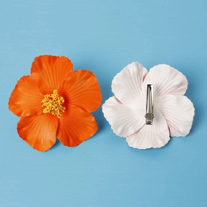 Detailed view of orange and white hibiscus flower hair clips on a blue background