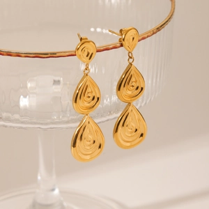 18K gold teardrop earrings with textured relief hang on a decorative glass rim