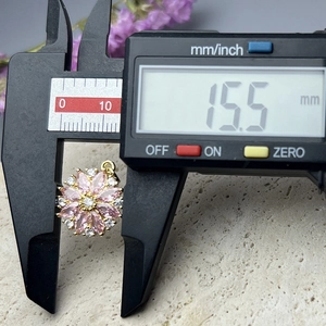 Macro shot showing digital caliper measuring a 15.5mm pink daisy pendant with zircons