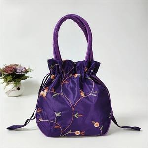 Detailed embroidery on a purple satin handbag with floral patterns and drawstring close