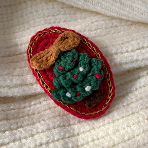 Macro detail of hand-knitted green Christmas tree hair clip with red beaded ornaments