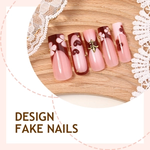 Pink French press-on nails with burgundy tips, white flowers, and golden metal charms