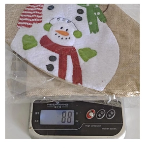 Detailed view of burlap Christmas snowman gift bag on an electronic scale weighing 88g