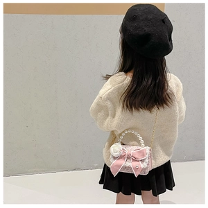 Detail view of a pink tweed girl's purse with a satin bow, camellia flower, and pearl handle