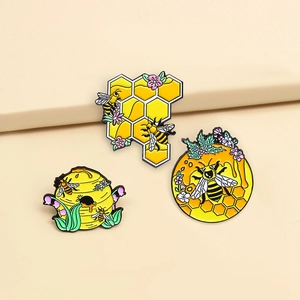 Detailed set of three bee and honeycomb enamel pins on a neutral beige background