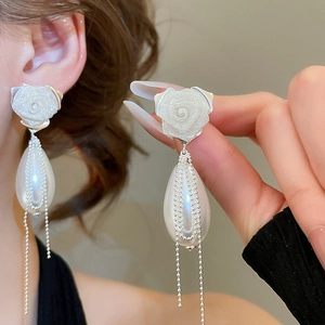 Detail of rose relief earrings with pear-shaped pearls and silver tassel chains on a model
