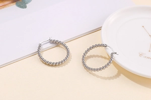 Detail of silver stainless steel hoop earrings with beaded texture on a white ceramic plate