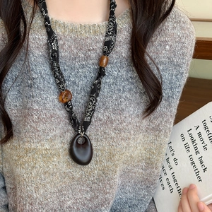 Detailed view of an ethnic fabric and wooden bead long necklace on a grey sweater