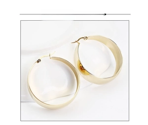 Detail of wide gold stainless steel hoop earrings with a polished mirror finish on white stand