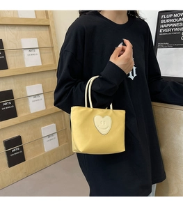Dettaglio di una borsa gialla con una toppa a cuore sorridente e manici sottili