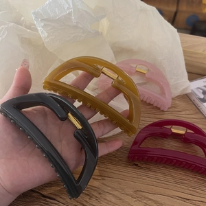 Detail of four colorful semi-circle hair claw clips in black, amber, pink, and burgundy