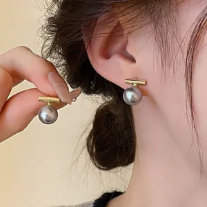 Détail de boucles d'oreilles barre dorée et perle grise portées à l'oreille, lumière douce