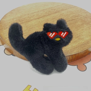 Detail of a black plush cat brooch featuring red heart-shaped glasses on a wood stand