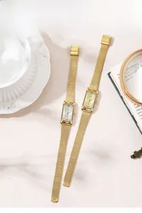 Lifestyle shot of gold rectangular quartz watches with mesh straps on a neutral book background