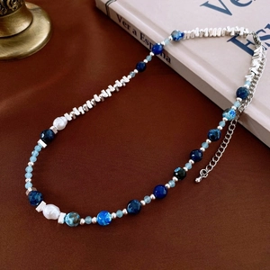 Artistic detail of beaded necklace with blue stones, pearls, and silver chain on vintage books
