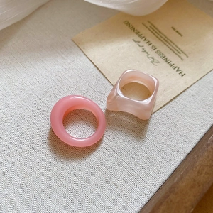 Detail of pink acrylic square and round rings set on a textured beige linen fabric