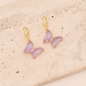 Detail view of gold butterfly earrings with purple and pink crystals on stone surface